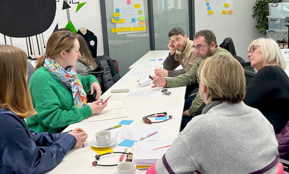 Photo from CDPS Standard Roadshow in Ynys Môn. A CDPS staff member and 5 people are sat around a table discussing the standards and taking notes.